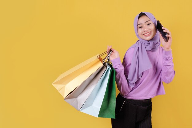 Beautiful asian woman showing shopping bags, wearing purple T shirt, using a mobile phone