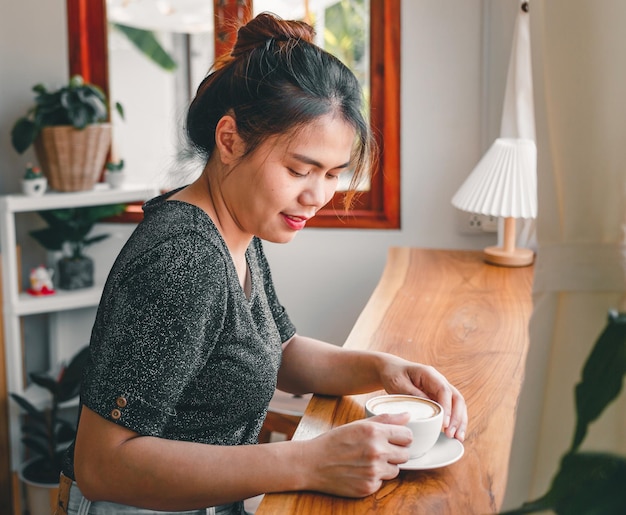 Bella donna asiatica si siede alla caffetteria con in mano una tazza di caffè sorridente rilassata nella caffetteria