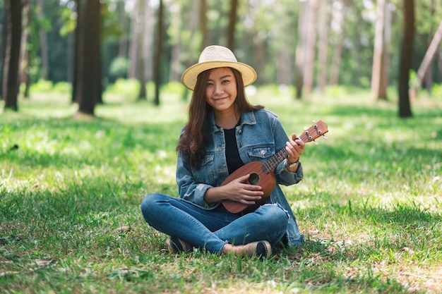 Una bella donna asiatica che si siede e che gioca ukulele nel parco