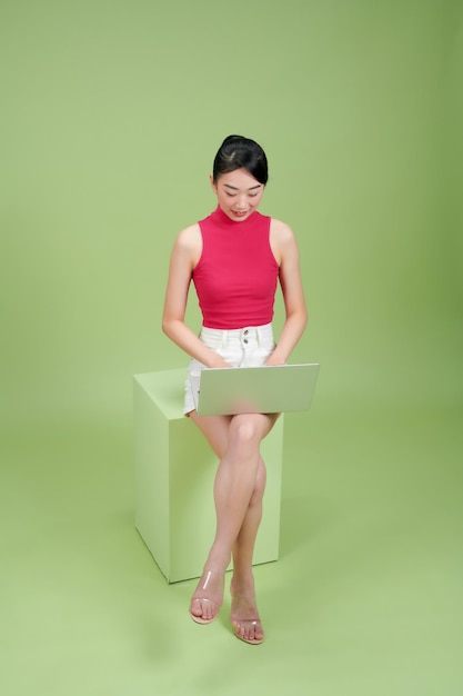 Photo beautiful asian woman sitting podium working with laptop isolated on green background