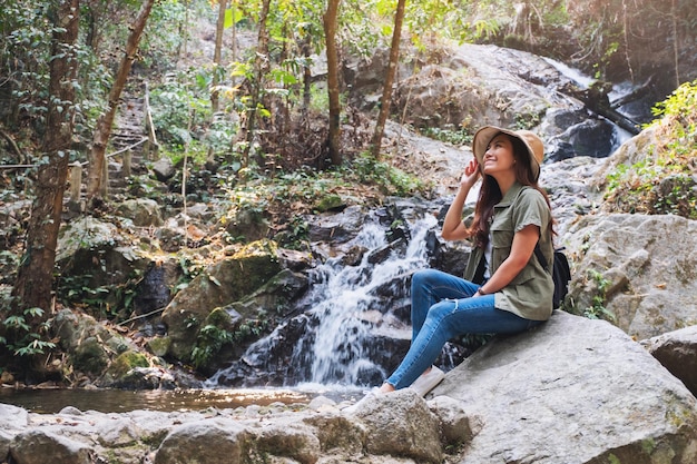 Una bella donna asiatica seduta sulla roccia davanti alla cascata