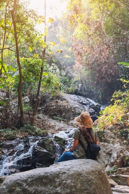 A beautiful asian woman sitting on the rock in front of waterfall