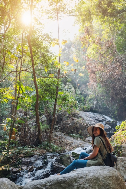 A beautiful asian woman sitting on the rock in front of waterfall