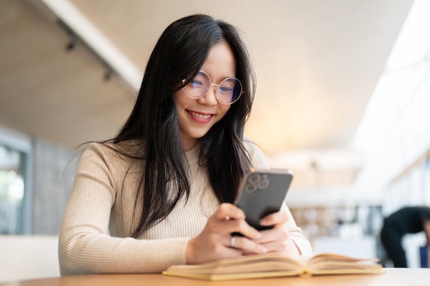 A beautiful Asian woman sitting at a table indoors and using her smartphone chat message