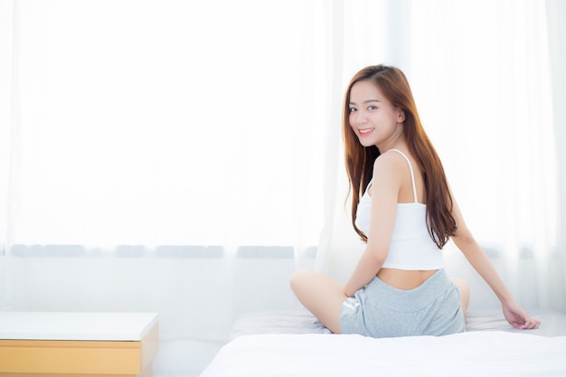 Bella donna asiatica che sorride con lo svago di felicità che si siede sul letto.