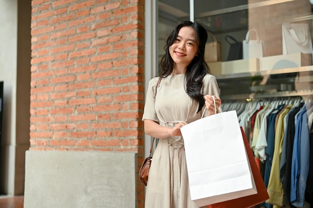 買い物袋を持って衣料品店の前に立つ美しいアジア人の女性