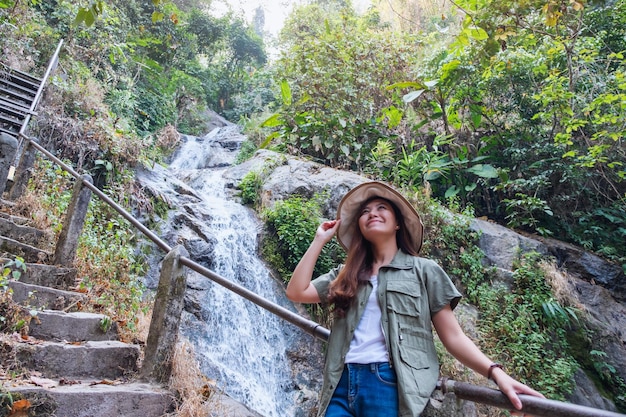 Una bella donna asiatica in piedi davanti alla cascata nella giungla