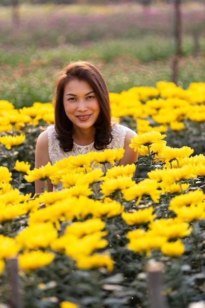 Bella donna asiatica in piedi e sorridente nel giardino fiorito tropicale con modo di felicità con la calda luce del sole dallo sfondo.