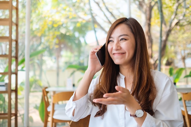Una bella donna asiatica che parla al cellulare con una faccia sorridente al bar