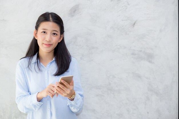 Beautiful asian woman talking phone and smile standing on cement background.