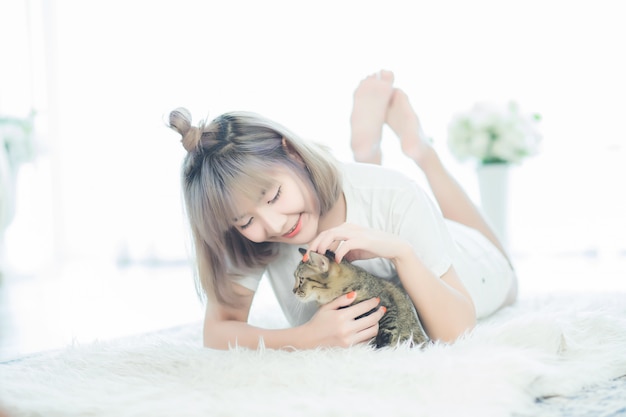 A beautiful Asian woman, Thai woman, wearing casual clothes, is lying with a cat on the carpet in the living room