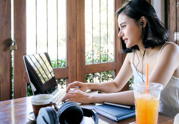 Bella donna asiatica che utilizza computer portatile al caffè, lavorando a casa concetto.