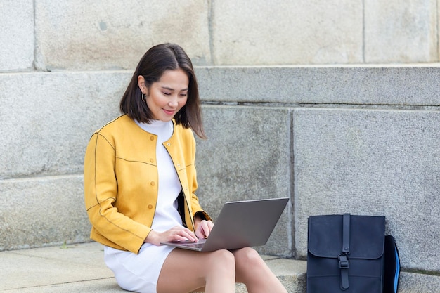 Beautiful asian woman using laptop computer. Smiling asian girl sitting on stairs and using a laptop. Asian business woman using laptop computer