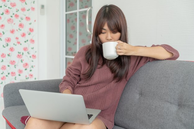 beautiful Asian woman using laptop on sofa in living room