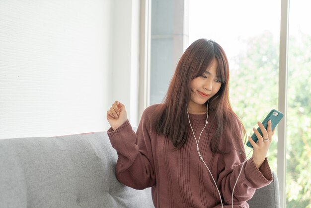 beautiful Asian woman using smartphone on grey sofa in living room