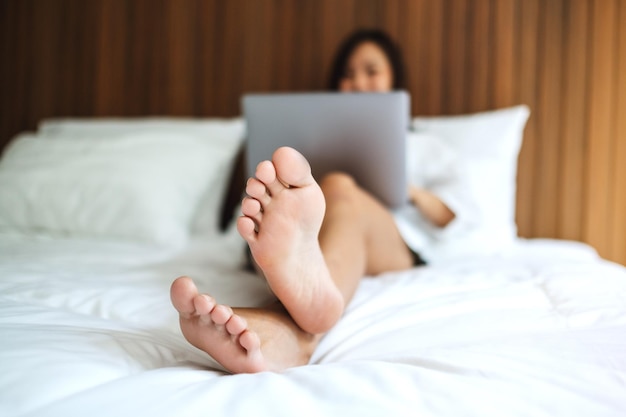 A beautiful asian woman using and working on laptop computer while lying on a white cozy bed at home