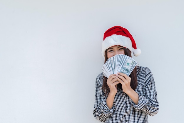 Beautiful asian woman wear santa hat with a lot money dollar in hand on white backgroundHappy woman conceptThailand people holding banknote