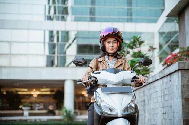 Beautiful asian woman wearing a helmet while riding a motorcycle with buildings in the background