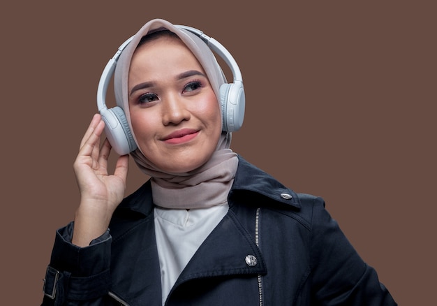 히잡을 쓴 아름다운 아시아 여성이 웃는 표정으로 무선 헤드폰을 사용하여 음악을 듣고 있었다