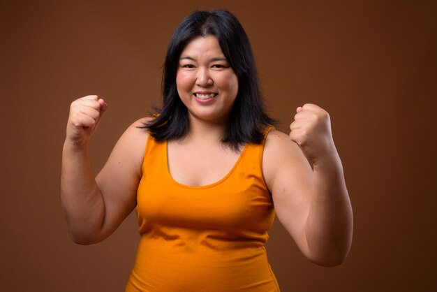 beautiful Asian woman wearing orange sleeveless dress on brown