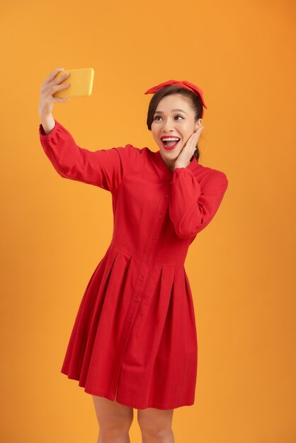 빨간 드레스를 입고 오렌지 배경 위에 서있는 아름다운 아시아 여자