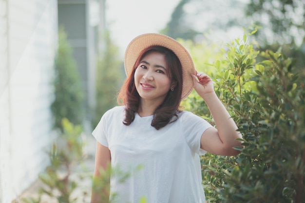 정원에서 웃는 얼굴 서 밀짚 모자를 쓰고 아름다운 아시아 여자