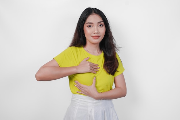Beautiful Asian woman wearing yellow shirt checking lumps on her breast for signs of breast cancer isolated by white background