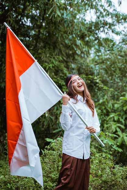 A beautiful asian woman in white shirt and brown skirt standing grab the indonesian flag at her hand