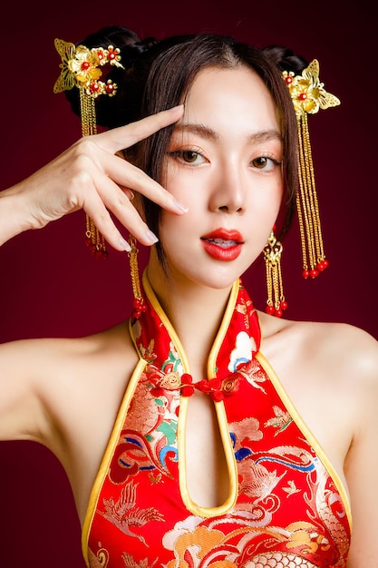 Beautiful Asian woman with clean fresh skin wearing cheongsam qipao dress touch her face on red background Portrait of female model in studio Happy Chinese new year