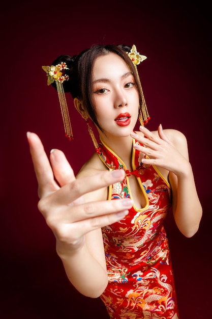 Beautiful Asian woman with clean fresh skin wearing cheongsam qipao posing on red background Portrait of female model in studio Happy Chinese new year