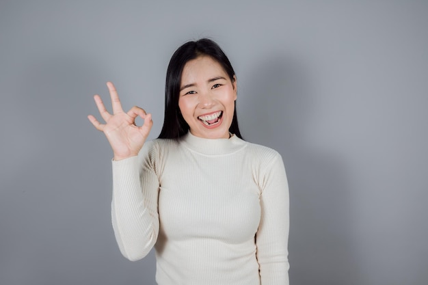 Beautiful Asian woman with long dark hair top showing oksign on gray background