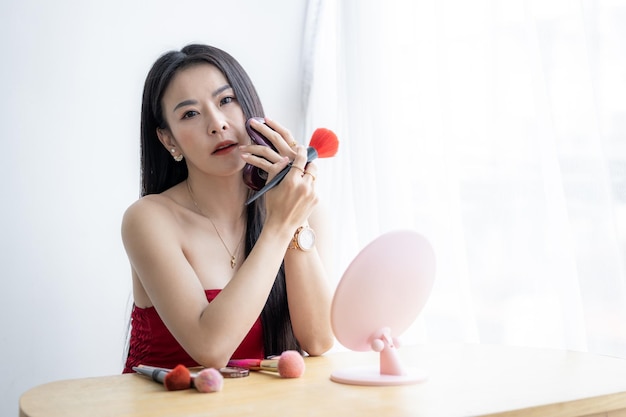 Beautiful asian woman with makeup brushes near face and look mirror Asian beauty make up Asian pretty girl holding make up brushes and make up on face with cosmetics set at home facial beauty