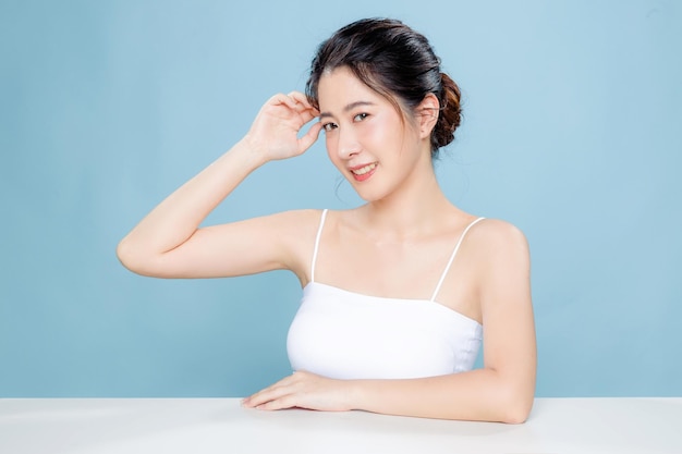 Beautiful Asian woman with perfect clear fresh skin Happy girl model with fresh glowing hydrated facial and natural makeup on blue background Cosmetology beauty and spa wellness Plastic surgery