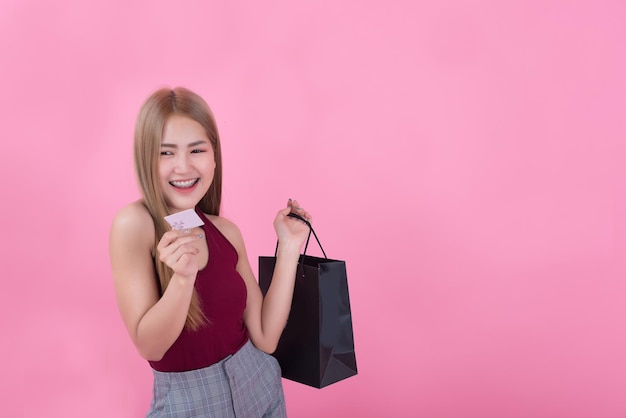 Beautiful asian woman with shopping bag and credit card in hand on pink backgroundThailand people is using a credit card and enjoys shopping