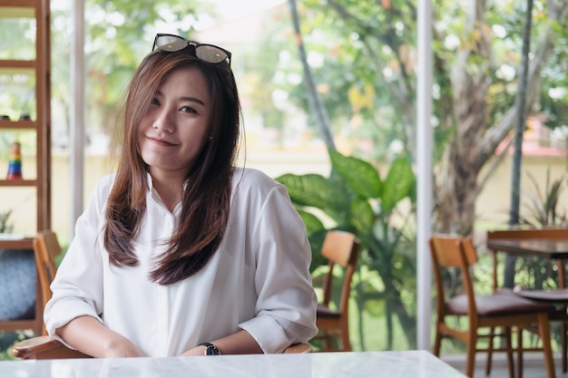 Beautiful Asian woman with smiley face and feeling good sitting in cafe with green nature 