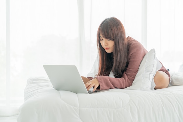 Bella donna asiatica che lavora con il computer portatile sul letto