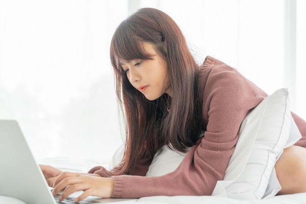 Beautiful asian woman working with laptop on bed