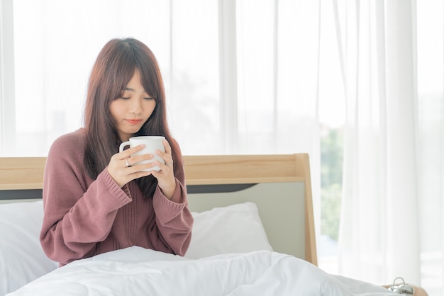 아침에 침대에서 커피를 마시는 아름다운 아시아 여성