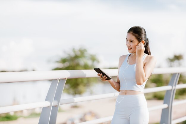 Photo beautiful asian women in sportswear listening to music during exercise outdoors in the park. healthy women concept. running workout.