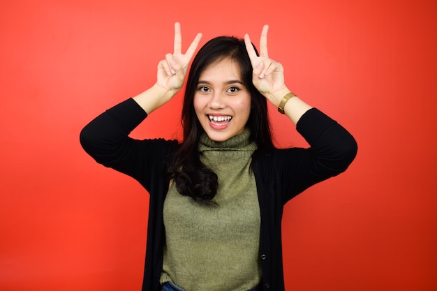 Photo beautiful asian women using black sweater fingers on head as bunny ears with red isolated background