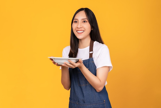 사진 아름다운 아시아 여성들은 노란색 배경에 흰색 접시를 들고 앞치마를 입는다