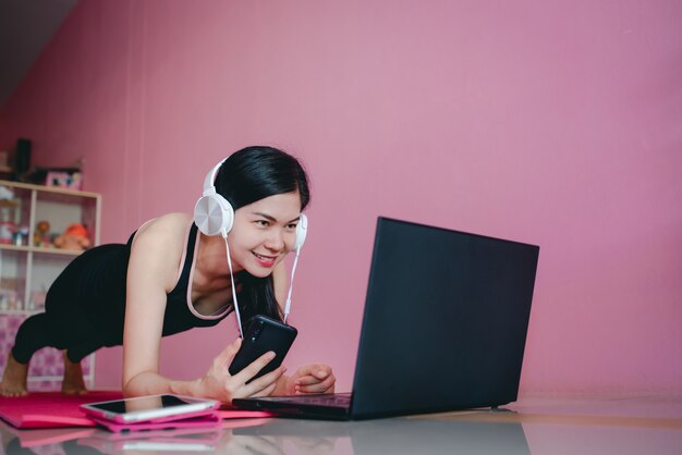 Beautiful asian women wear headphones, exercise in black sportswear, lie down, watch home exercise videos and notebook computers.