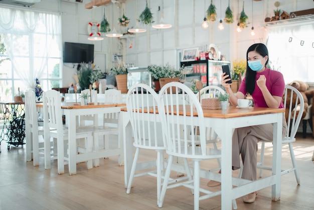 Beautiful Asian women wearing masks Work online at a coffee shop She freely sells products online, enjoys working at home during the Covid-19 infection.