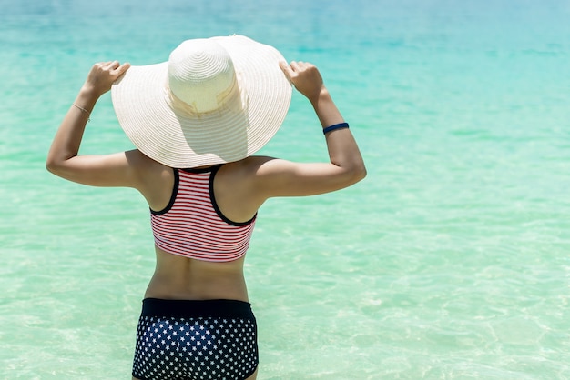 Beautiful Asian women wearing summer hat and bikini enjoying a holiday on the sea shore