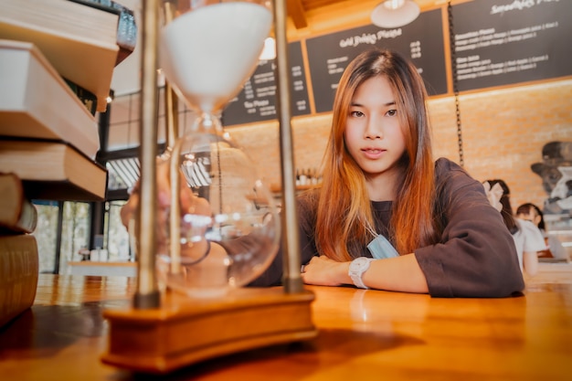 Foto la bella giovane femmina asiatica è seduta davanti a una clessidra che fa il conto alla rovescia con un sorriso per il concetto di tempo rilassante.