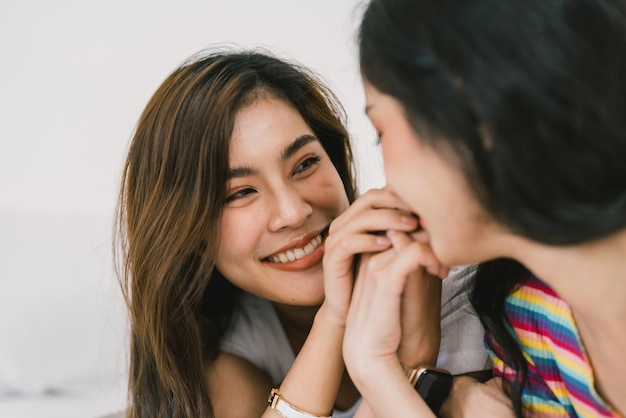 Beautiful asian young lesbian LGBTQ couple or friends using computer laptop together smile and relax on bedHappiness LGBTQ couple woman spending time together at home LGBTQ Pride Month Concept