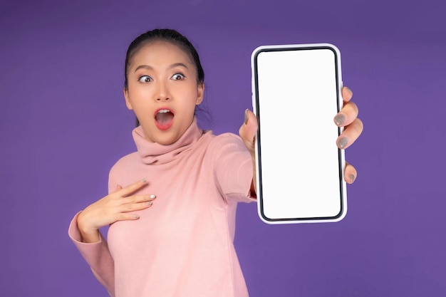 Beautiful asian young woman excited surprised girl showing smart phone with blank screen white screen isolated on purple background mock up image