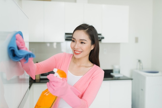 Bella giovane donna asiatica in guanti protettivi che pulisce l'armadio da cucina