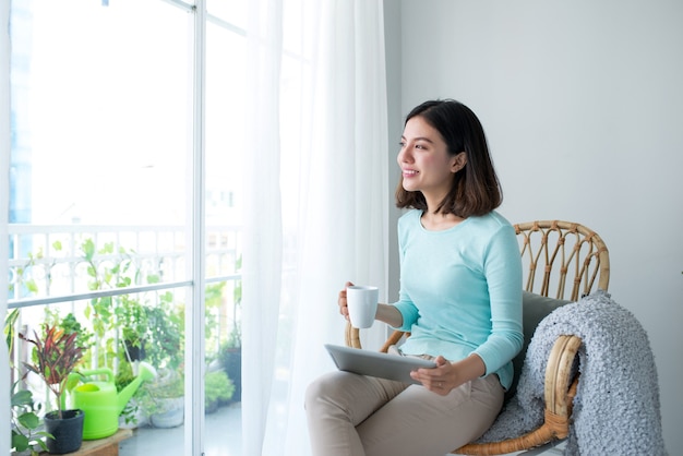 リラックスして自宅でデジタルタブレットを使用して美しいアジアの若い女性