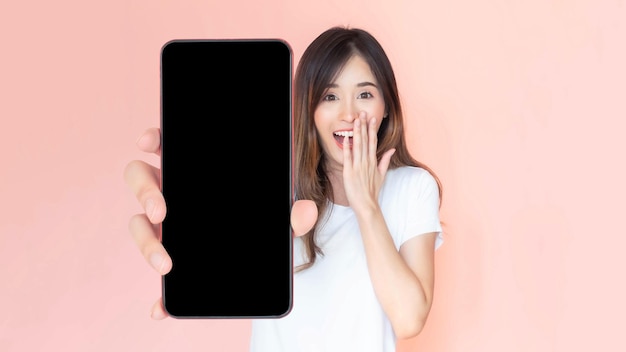 분홍색 배경에 격리된 광고 배너를 위한 빈 화면 흰색 화면 빈 복사본 공간이 있는 큰 스마트폰을 보여주는 아름다운 아시아 젊은 여성